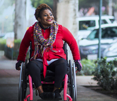 woman on city sidewalk in wheelchair smiling