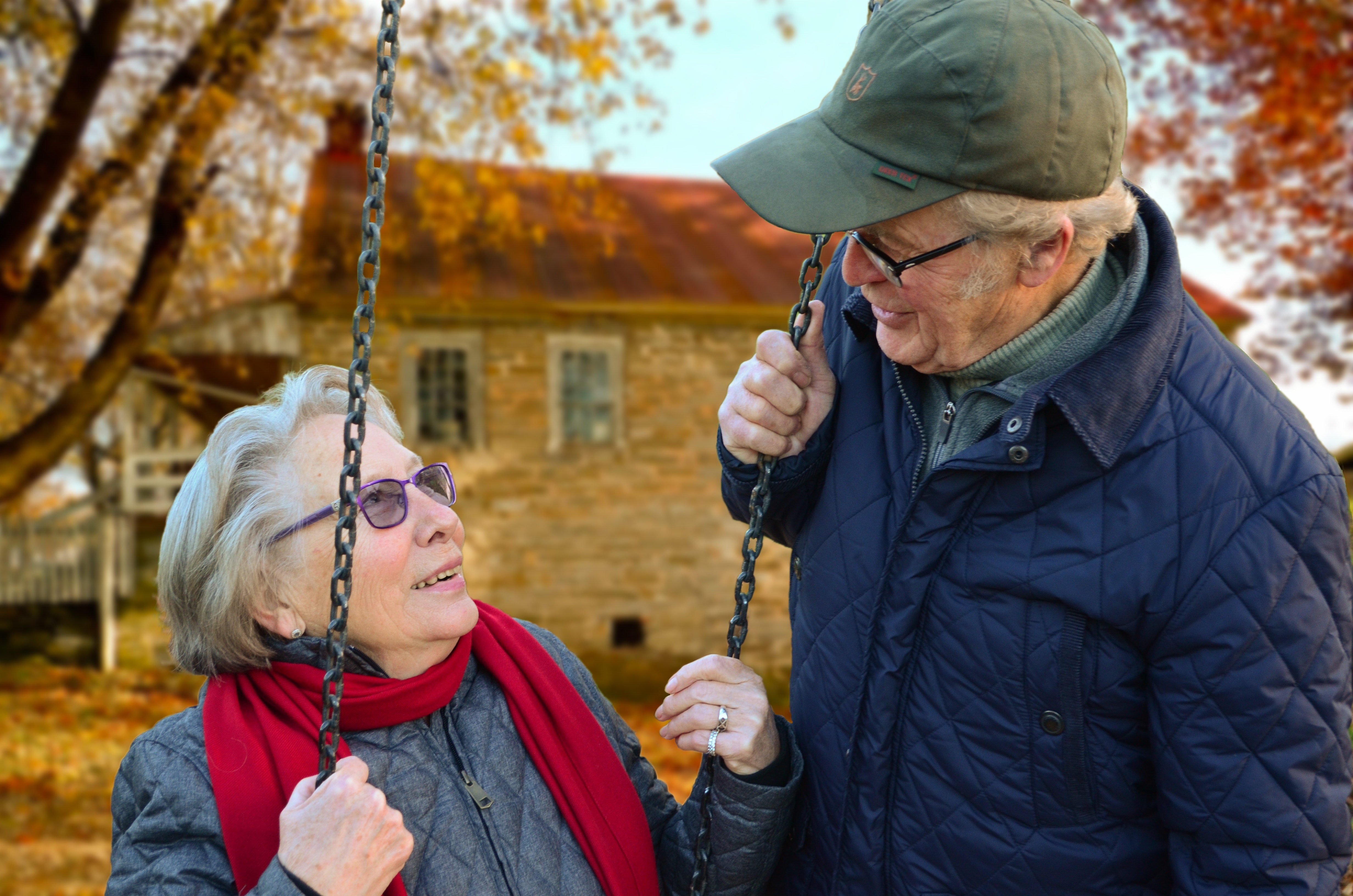 Senior couple talking while woman is seated on a swing, on an autumn day
