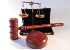 A judge's gavel and mallet displayed in front of the scales of justice, sitting inside of a black briefcase