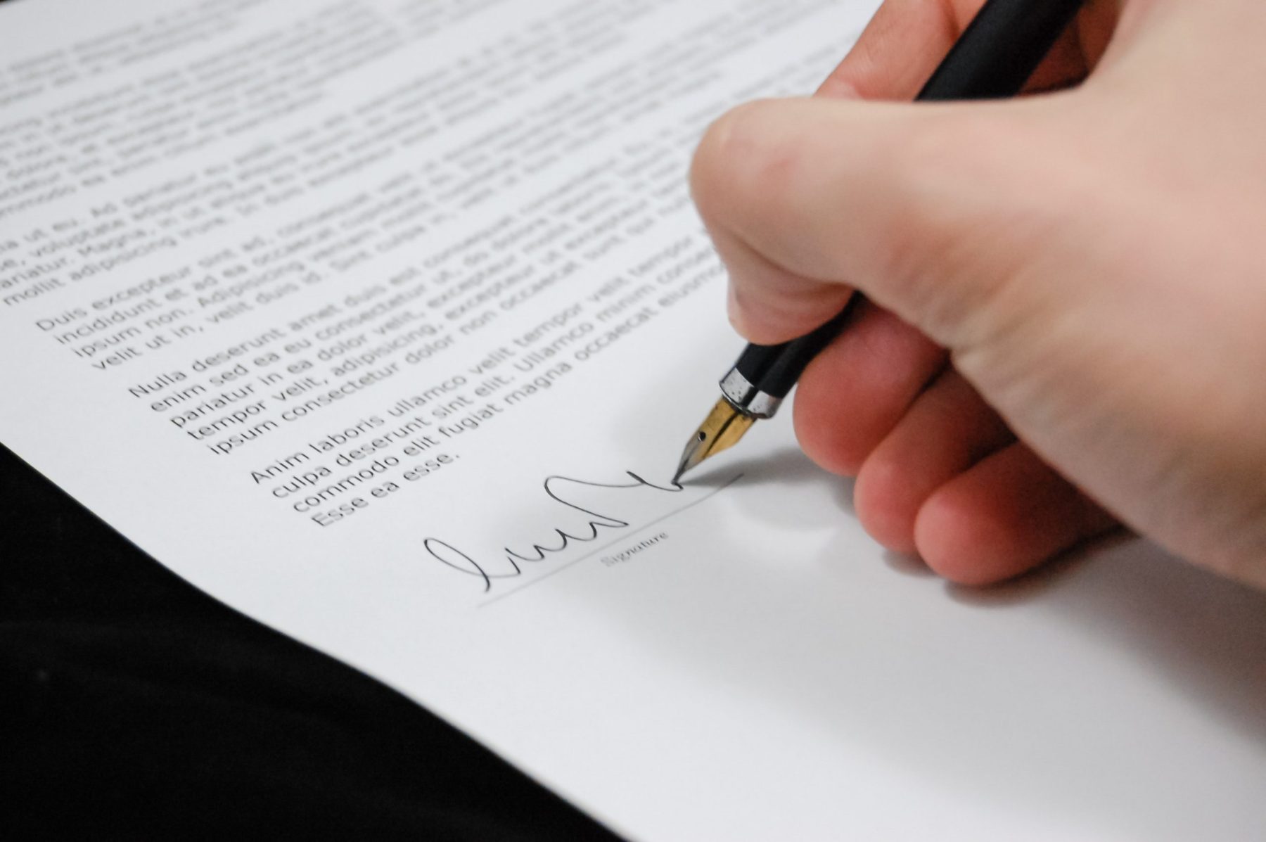 A person's hand signing a business document at the bottom of the page.