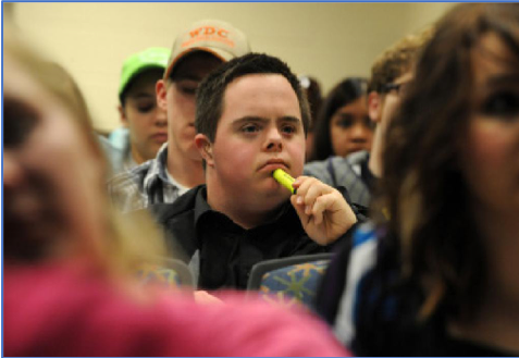 Student with developmental disabilities listening attentively with a yellow highlighter in hand, sitting in a classroom full of students